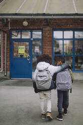 Rear view of boys with arm around walking towards school building - MASF30120