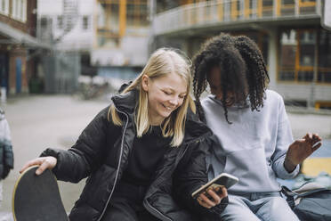 Glückliche Mädchen zeigen einem Freund auf dem Schulgelände ihr Smartphone - MASF30127