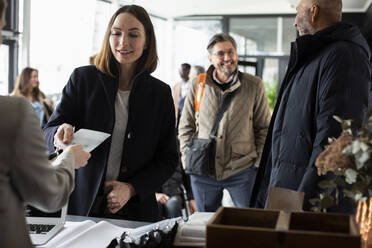 Geschäftsfrau nimmt Ausweis von Empfangsdame an Anmeldeschalter in Kongresszentrum - MASF30134