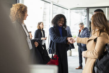 Lächelnde Geschäftsfrau beim Händeschütteln mit einer weiblichen Fachkraft bei einem Seminar im Kongresszentrum - MASF30143