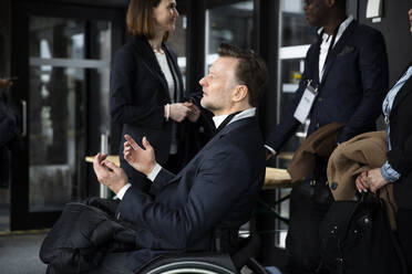 Seitenansicht eines behinderten Geschäftsmannes, der im Rollstuhl sitzend vor Seminarteilnehmern gestikuliert - MASF30177