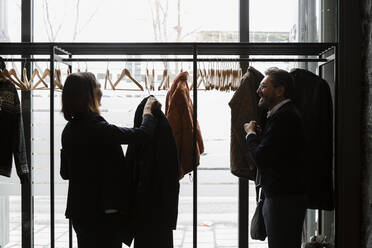 Seitenansicht von Geschäftsleuten, die sich unterhalten, während sie ihre Mäntel auf einem Gestell im Konferenzzentrum aufhängen - MASF30185