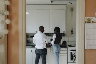 Rear view of father and daughter doing household work in kitchen - MASF30264