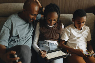 Father sitting with daughter and son using wireless technologies at home - MASF30272
