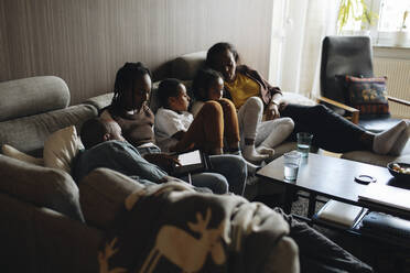 Father and mother relaxing with children on sofa in living room at home - MASF30274