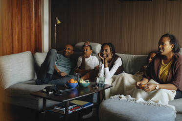 Familie sieht gemeinsam fern, während sie zu Hause auf dem Sofa sitzt - MASF30276