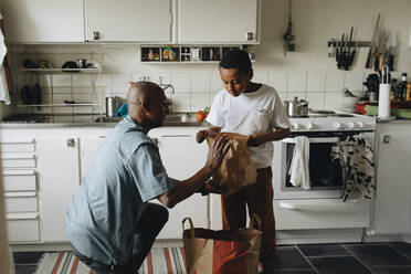 Father and son searching in paper bags in kitchen at home - MASF30290