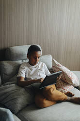 Boy using tablet PC while sitting on sofa at home - MASF30312