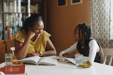 Glückliche Tochter sieht Mutter lachend an, während sie am Tisch sitzt - MASF30316