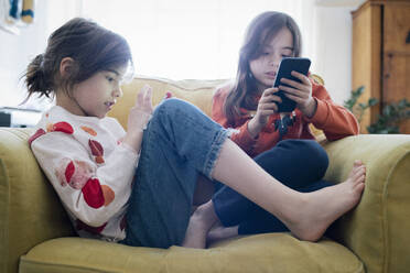 Mädchen, das ein Mobiltelefon benutzt, sitzt mit ihrer Schwester auf einem Sessel zu Hause - MASF30333
