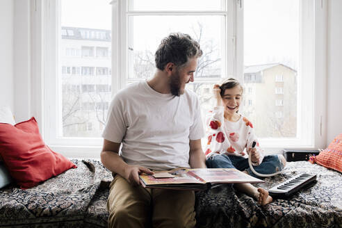 Glücklicher Mann sieht seine Tochter an, die zu Hause auf dem Bett sitzt und Klavier spielt - MASF30334