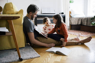 Mädchen, das seine Schwester beim Lesen eines Buches beobachtet, die mit ihrem Vater zu Hause im Wohnzimmer sitzt - MASF30335