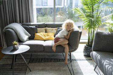 Smiling girl sitting on sofa at home - SVKF00183