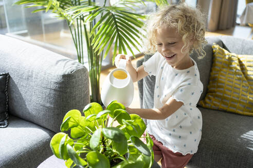 Lächelndes Mädchen mit blondem Haar bewässert Pflanze zu Hause - SVKF00185