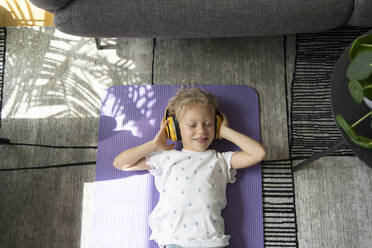 Girl listening music through headphones lying on exercise mat at home - SVKF00195