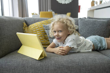 Lächelndes Mädchen auf dem Sofa liegend mit Tablet-PC zu Hause - SVKF00199