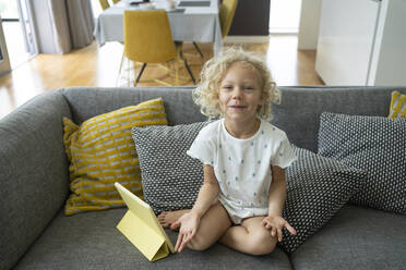 Lächelndes Mädchen mit Tablet-PC sitzt inmitten von Kissen auf dem Sofa zu Hause - SVKF00202