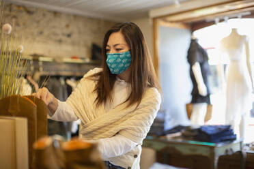 Female shop owner in face mask arranging display in boutique - CAIF32681