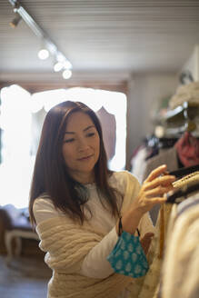 Female shopper with face mask looking at clothing in boutique - CAIF32687