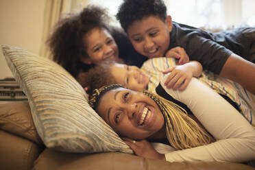 Happy playful mother and children cuddling on living room sofa - CAIF32718