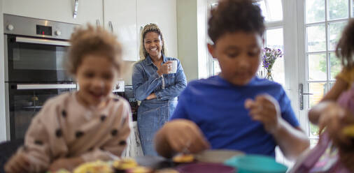 Glückliche Mutter beobachtet Kinder beim Backen in der Küche - CAIF32728