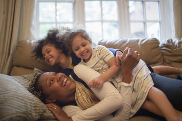 Happy playful mother and daughters on living room sofa - CAIF32740