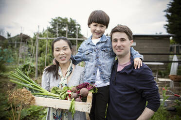 Porträt einer glücklichen Familie mit geerntetem Gemüse im Garten - CAIF32744