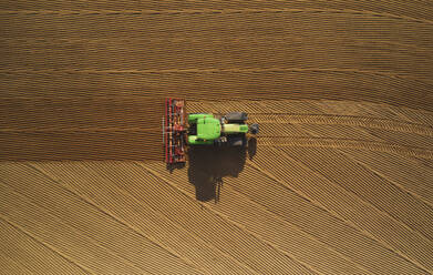 Aerial view of a green tractor plowing the arid soil in a paddy in the Lomellina region, Po Valley, Italy. - AAEF14655