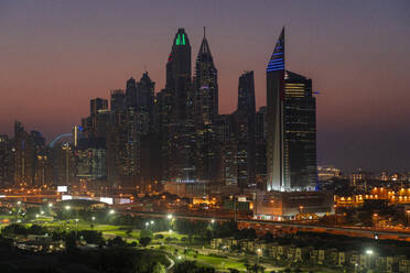 Vereinigte Arabische Emirate, Dubai, Beleuchteter Golfplatz bei Nacht mit Jumeirah Lakes Towers im Hintergrund - TAMF03378
