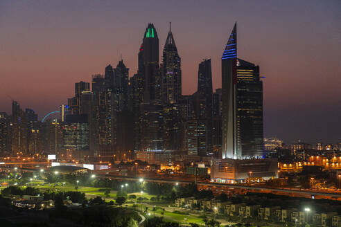 Vereinigte Arabische Emirate, Dubai, Beleuchteter Golfplatz bei Nacht mit Jumeirah Lakes Towers im Hintergrund - TAMF03378