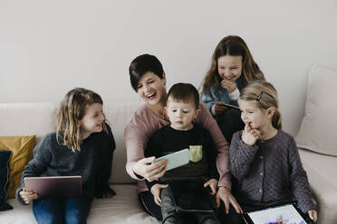 Happy family with wireless technology sitting together on sofa at home - LHPF01449