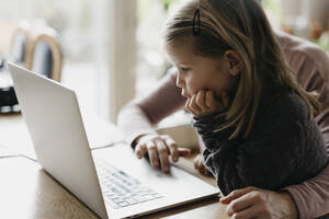 Mädchen mit Hand am Kinn, das auf einen Laptop schaut und mit seiner Mutter sitzt - LHPF01453
