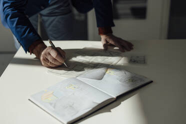 Hands of businessman drawing blueprint at desk in office - JOSEF09691