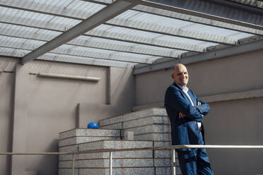 Smiling architect with arms crossed standing at construction site - JOSEF09698