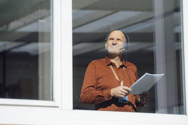 Businessman wearing headset holding document seen through glass - JOSEF09711