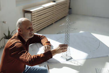 Businessman examining electricity pylon model on blueprint at desk - JOSEF09725