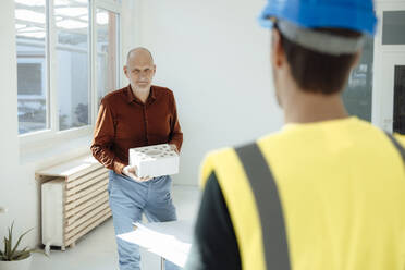 Businessman holding concrete brick discussing with colleague in office - JOSEF09735