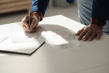 Hand of businessman holding pen on blueprint at desk - JOSEF09770