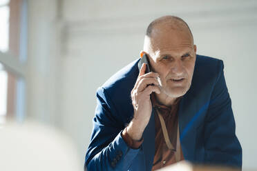 Businessman talking on mobile phone in office - JOSEF09817