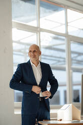 Smiling senior architect buttoning blazer in office - JOSEF09849