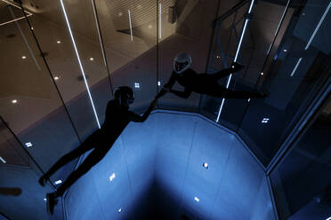 Athletes holding each others hands flying in illuminated wind tunnel - MRRF02117