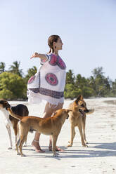 Frau mit ausgestreckten Armen neben Hunden am Strand stehend - NDF01449