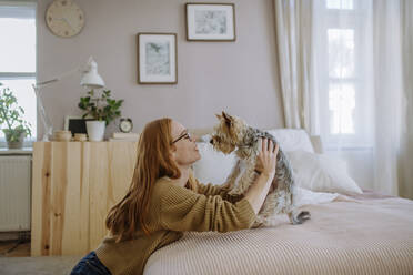 Lächelnde Frau mit Hund, die sich zu Hause auf das Bett lehnt - HAPF03101