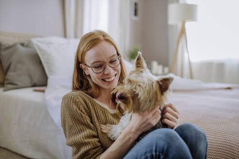 Fröhliche Frau mit Hund zu Hause am Bett sitzend - HAPF03105