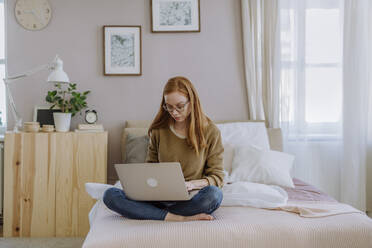 Frau mit Laptop im Schneidersitz auf dem Bett zu Hause - HAPF03109