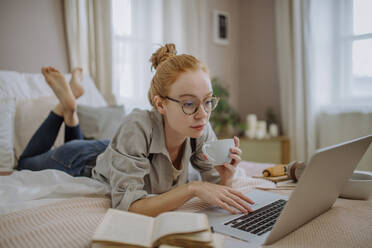 Student mit Kaffeetasse und Laptop auf dem Bett liegend zu Hause - HAPF03151