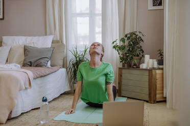 Frau, die zu Hause mit Hilfe eines Laptops E-Learning für Yoga praktiziert - HAPF03166