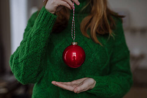 Frau mit grünem Pullover hält roten Weihnachtsschmuck zu Hause - HAPF03174