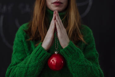 Frau mit rotem Weihnachtsschmuck stehend vor schwarzem Hintergrund - HAPF03175