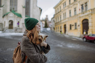 Woman wearing knit hat carrying Yorkshire Terrier in city - HAPF03189